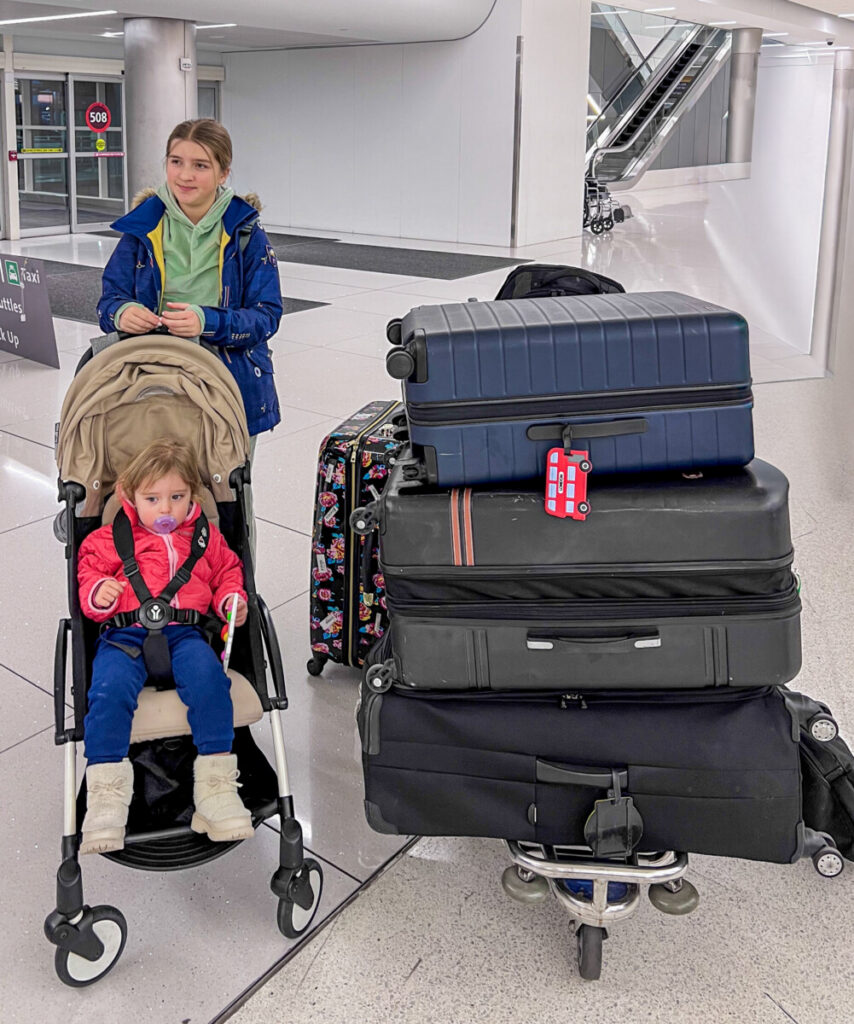 two girls, one tween one in stroller at airport with lots of suitcases