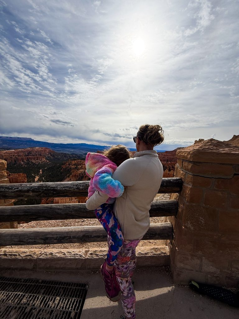 Mom holding daughter at a Bryce Canyon with kids overlook, hoodoos visible below