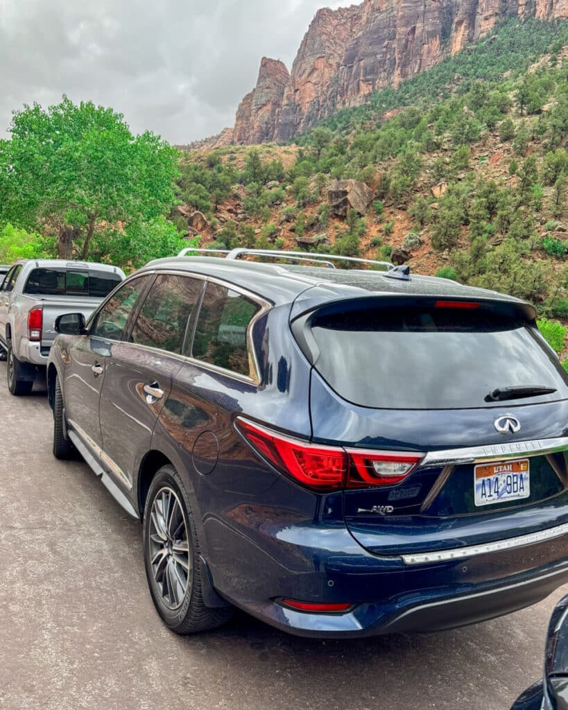 Car parked in a Zion National Park pullout with towering canyon walls in the background