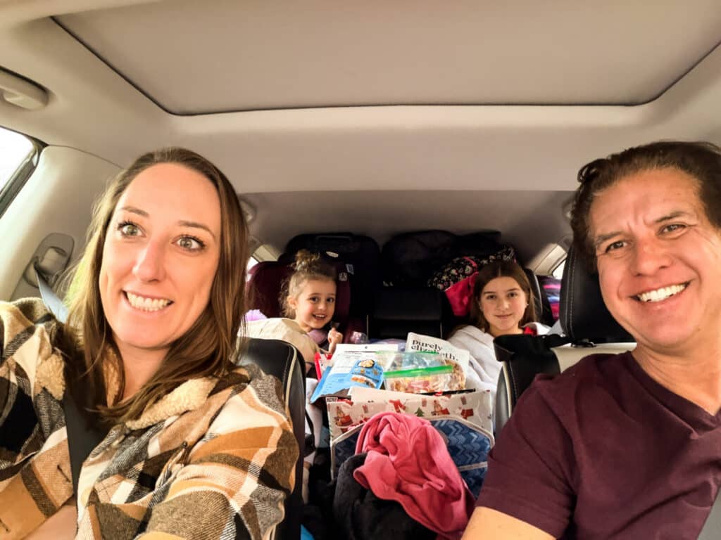 Family of four smiling in a packed car on a Utah parks road trip