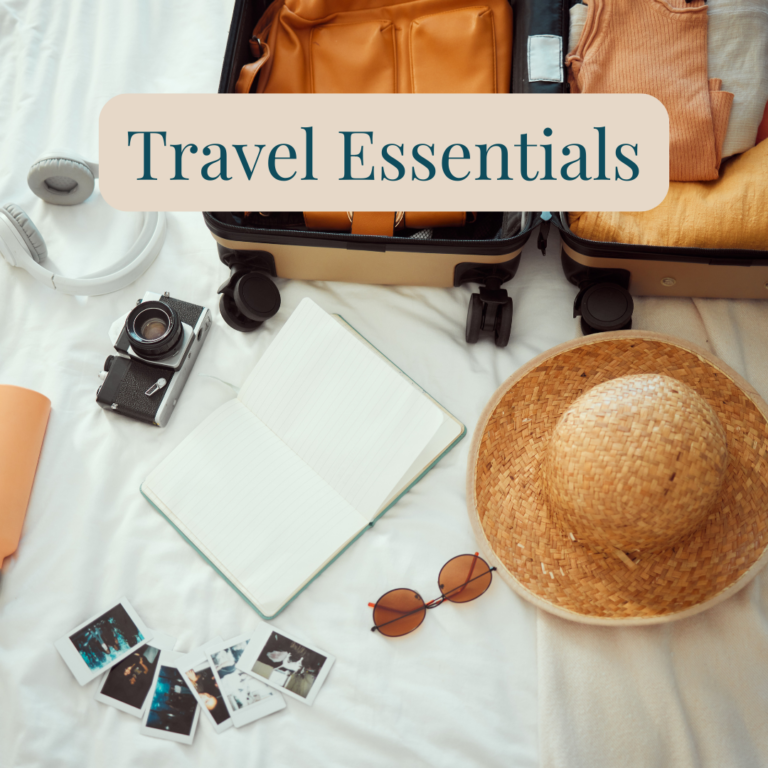 Open suitcase with clothes, headphones, camera, notebook, sunglasses and a straw hat.
